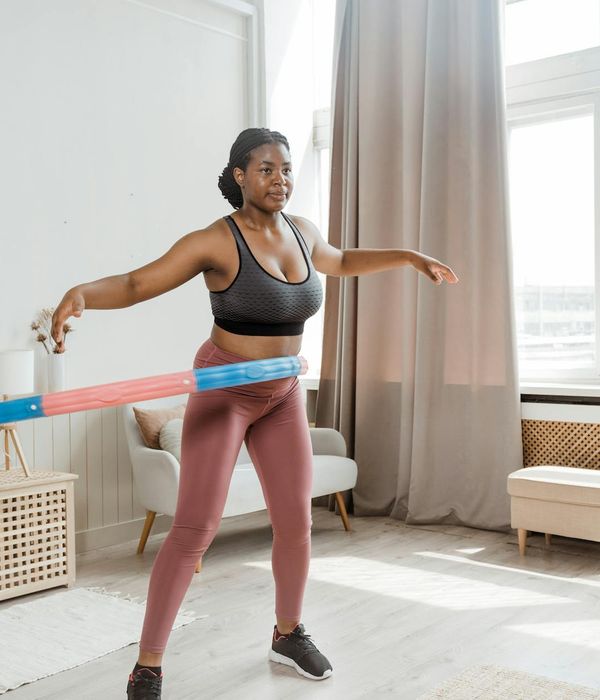 Smiling woman in sportswear performing a light cardio movement in a modern, bright room.